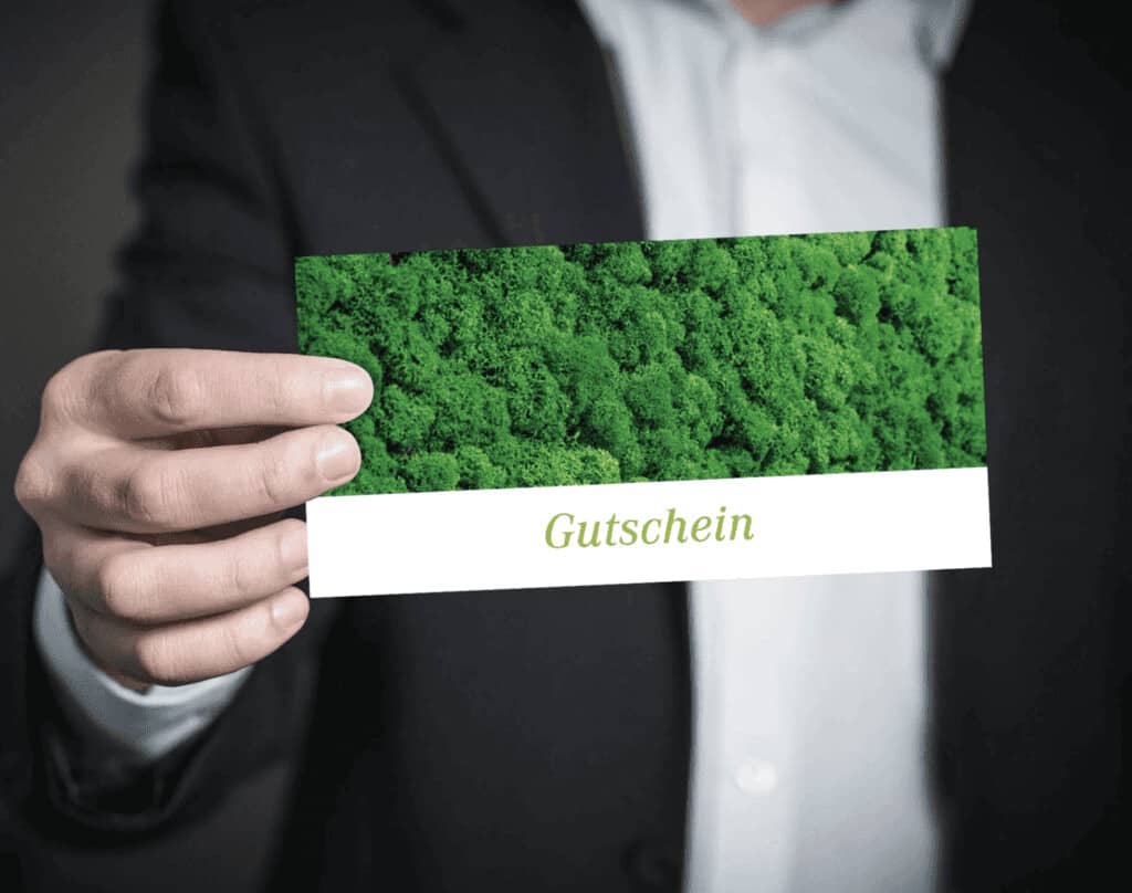 Hand hält einen Gutschein des Grünen Hotels zur Post mit Moos-Motiv