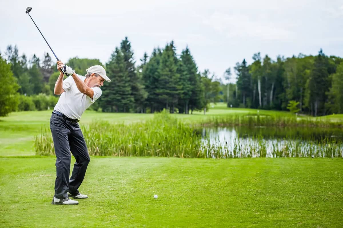 Golfer beim Abschlag auf einem Golfplatz mit Teich und Wald