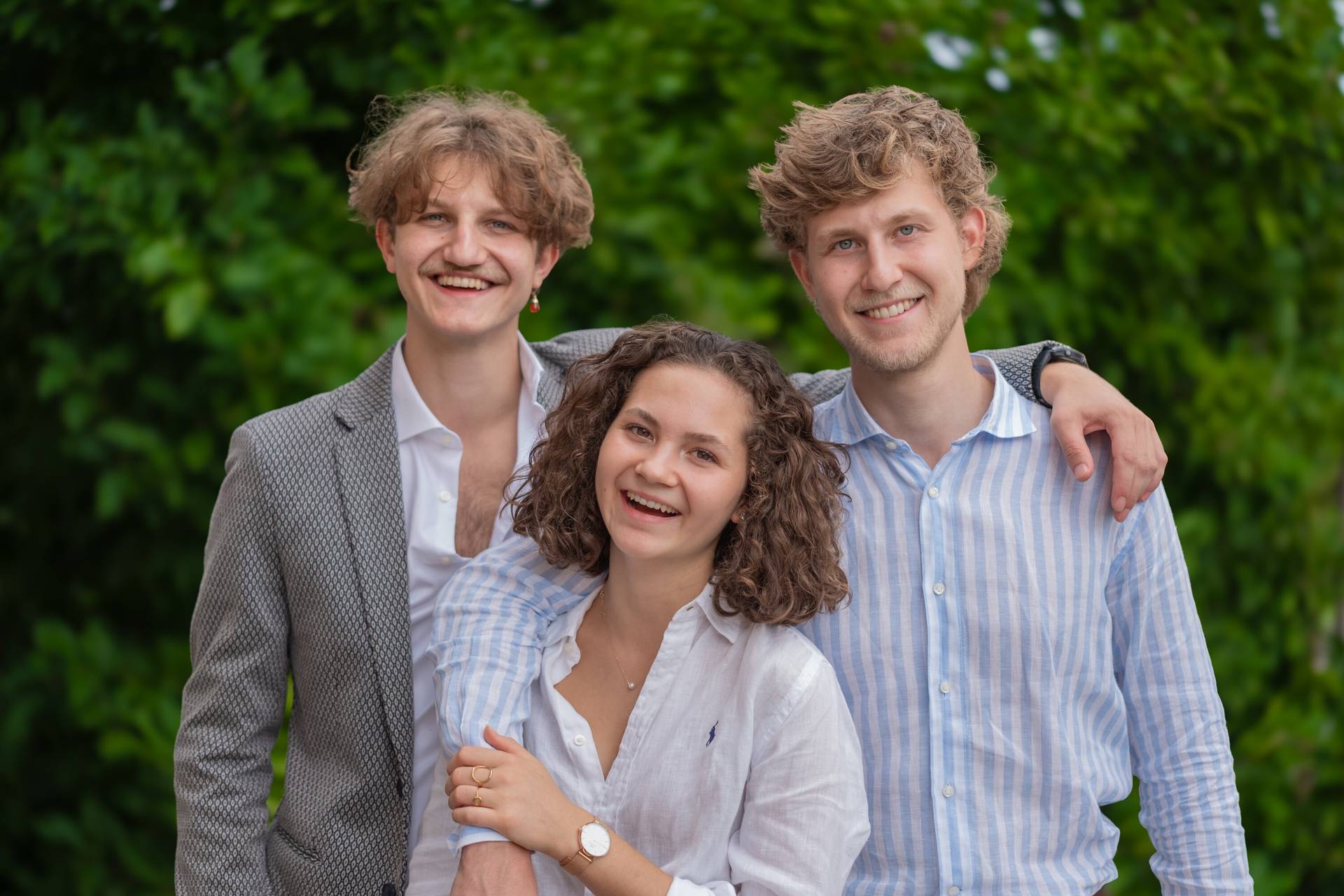 Markus, Paul und Romy lachend vor einer grünen Hecke
