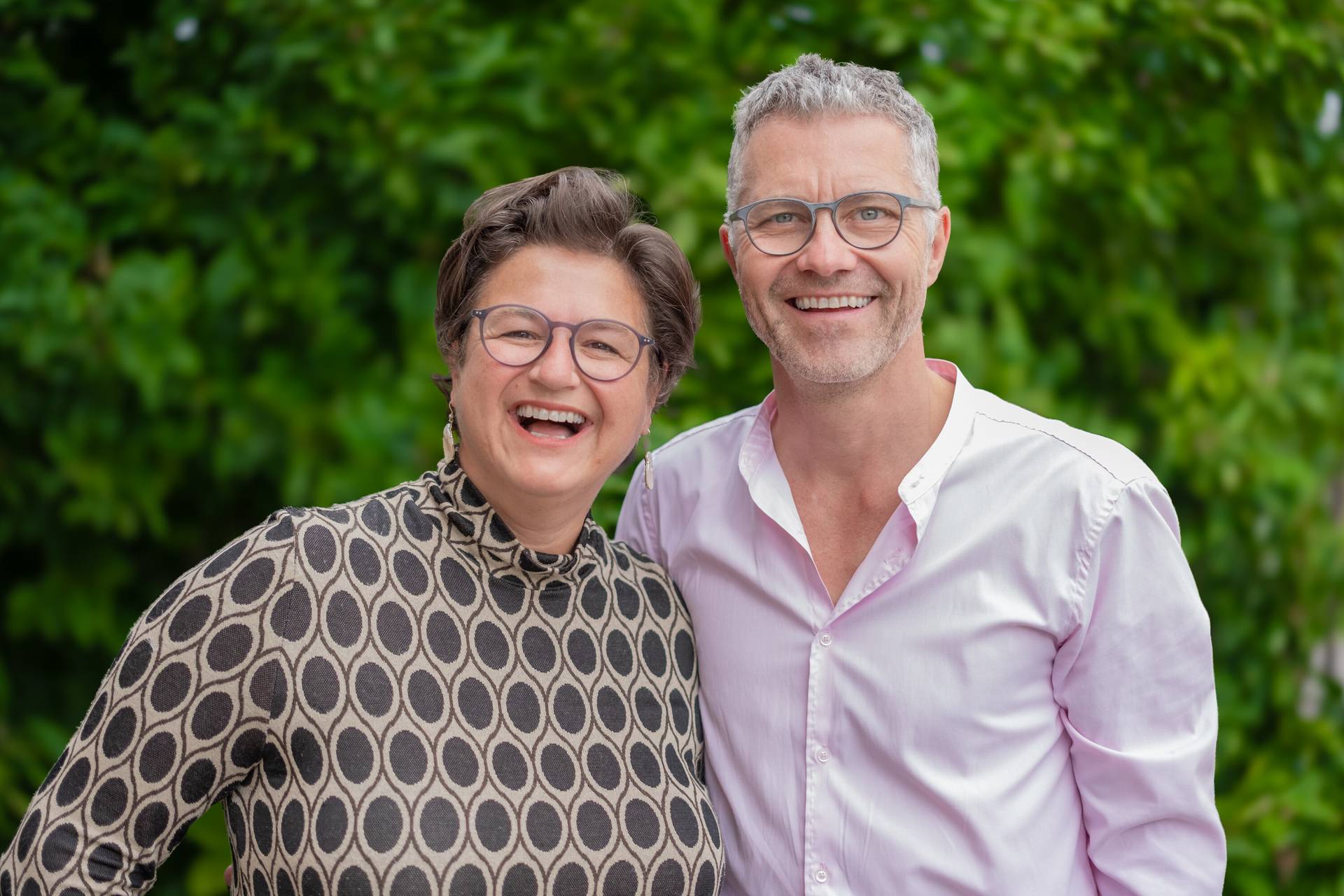 Silvia und Georg Maier lachend vor einer grünen Hecke