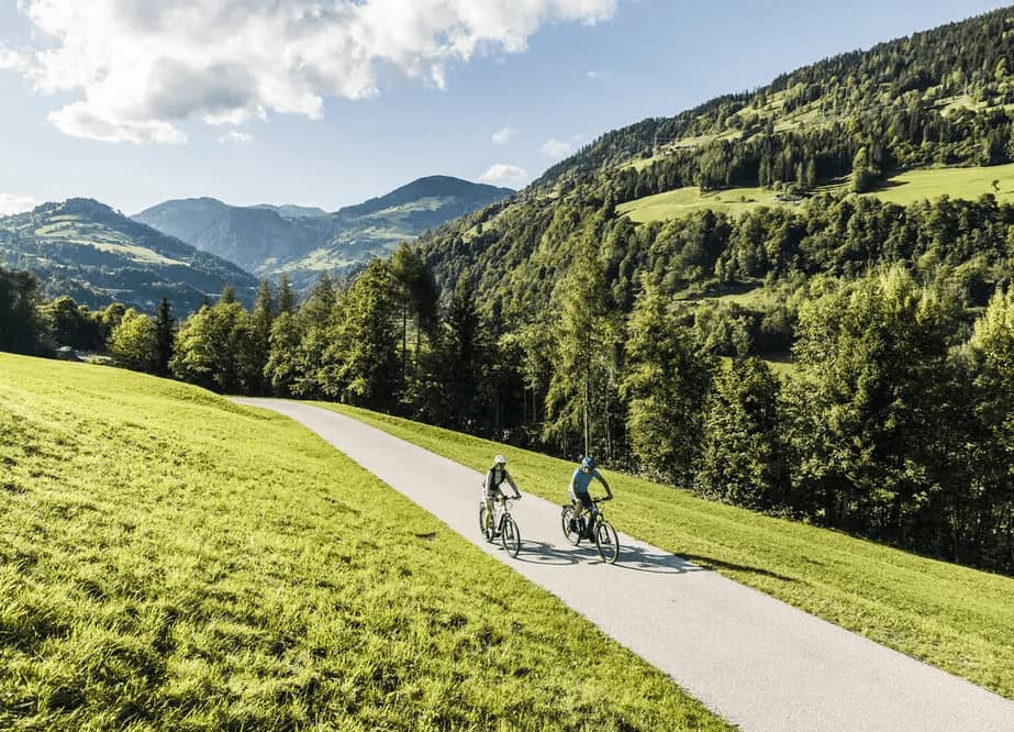 Zwei Radfahrer auf einem Weg durch grüne Wiesen in den Bergen