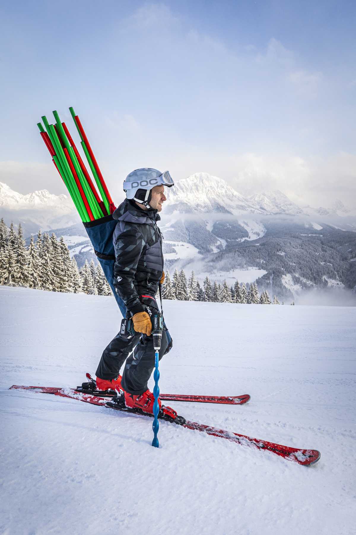 Hochformat: Skilehrer mit Torstangen auf dem Rücken vor Bergpanorama