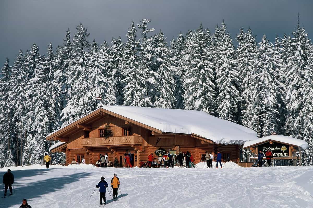Das Blockhaus der Kleinbergalm im Schnee, Skifahrer davor, tief verschneiter Wald