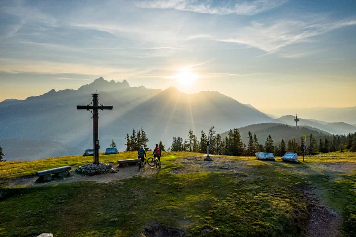 Gipfelkreuz am Rossbrand im Abendlicht, zwei Mountainbiker, dahinter die Bischofsmütze