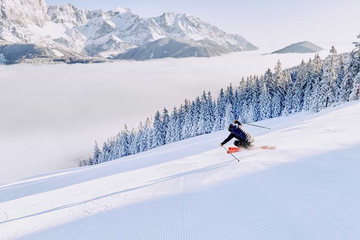 Skifahrerin carvt auf frisch präparierter Piste, dahinter Nebelmeer und Bergmassiv