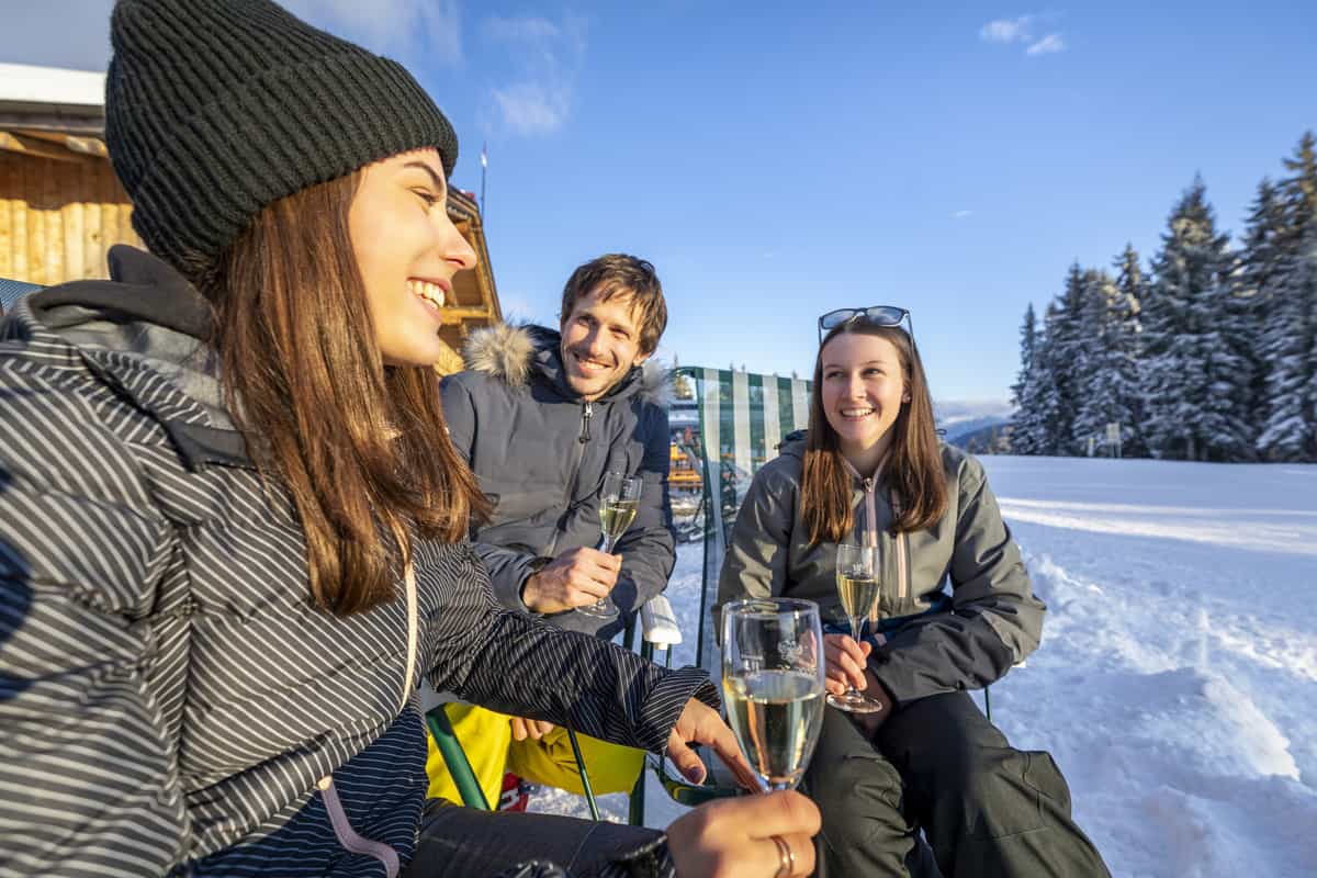 Drei Freunde mit Sektgläsern im Schnee vor der Hütte, lachend