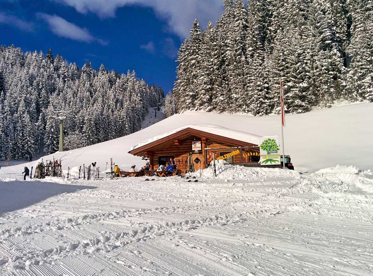Die Holzwurmhütte an der Piste, Gäste auf der Terrasse, verschneiter Wald