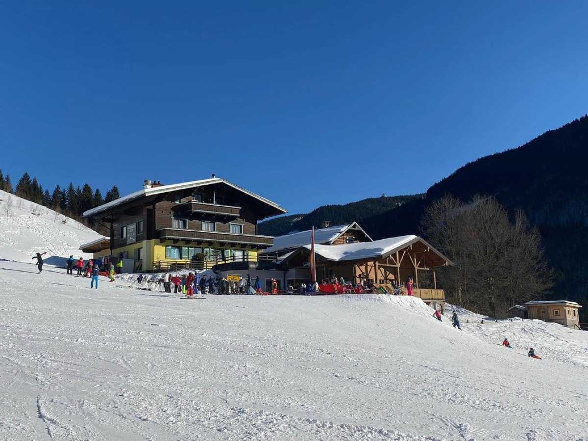 Die Geierbergalm an der Piste, Skifahrer vor der Terrasse, blauer Himmel
