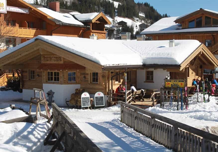 Der Alm Stadl mit verschneiter Terrasse, dahinter verschneite Häuser
